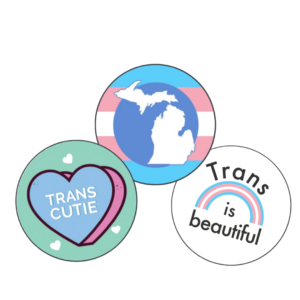 3 buttons, one with a heart that reads "Trans Cutie," one with a silhouette of Michigan in trans colors, and one with a trans rainbow that reads "Trans is Beautiful"