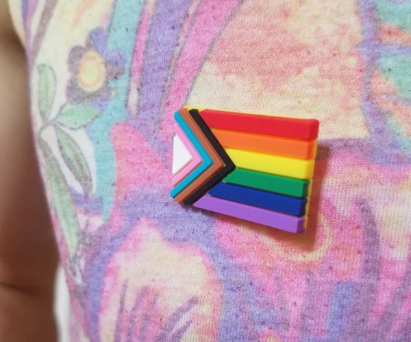 A progress pride lapel pin on a lightly floral shirt.