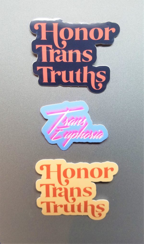 Three stickers. One is dark blue vinyl sticker that says Honor Trans Truths in an deep coral embellished font. The second is light blue vinyl stickers that say Trans Euphoria in bright white scrawling text with a bright pink shadow. The third is a cream colored vinyl sticker that says Honor Trans Truths in an burnt orange embellished font.